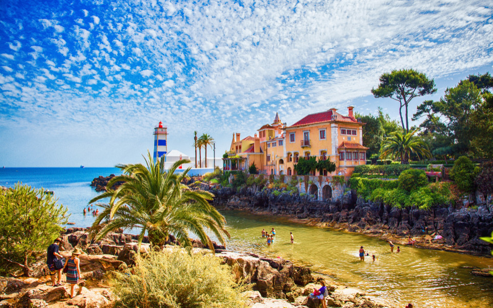 Malerische K&uuml;stenlandschaft in Cascais mit dem Phare du Farol de Santa Marta, idyllischer Bucht, Palmen und charmanten Villen am azurblauen Atlantik.